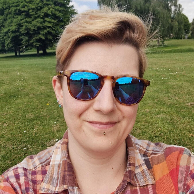 A smiling white person with short blonde hair and glasses.